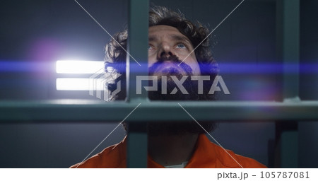 Male criminal holds metal bars with handcuffed hands 105787081