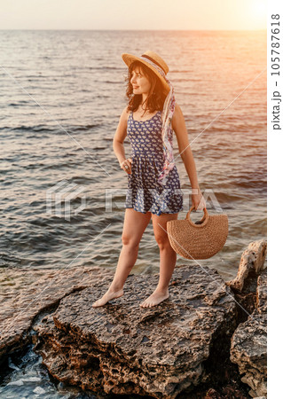 A woman in a dress, hat and with a straw bag is standing on the 105787618