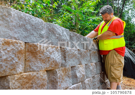 Construction worker skillfully fastened concrete block in place on retaining wall. Construction worker skillfully fastened concrete block in place on retaining wall. 105790878