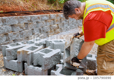 Construction worker lifts concrete block and places it on retaining wall Construction worker lifts concrete block and places it on retaining wall 105790890