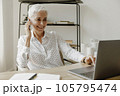 Smiling stylish mature woman sitting at desk with laptop and talking on mobile phone. 105795474