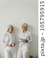 Senior females drinking coffee and laughing on white wall background. 105795915