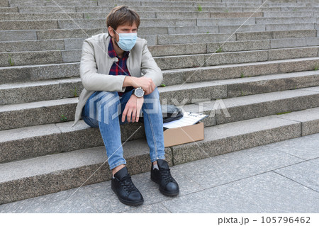 Unhappy sad business man in medical mask sitting on the stairs outdoors Unhappy sad business man in medical mask sitting on the stairs outdoors 105796462