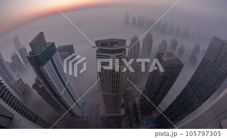 Rare early morning winter fog above the Dubai Marina skyline and skyscrapers lighted by street lights aerial night to day timelapse. Rare early morning winter fog above the Dubai Marina skyline and skyscrapers lighted by street lights aerial night to day timelapse. 105797305