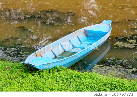 The muddy riverbank hosts a blue boat. The muddy riverbank hosts a blue boat. 105797872