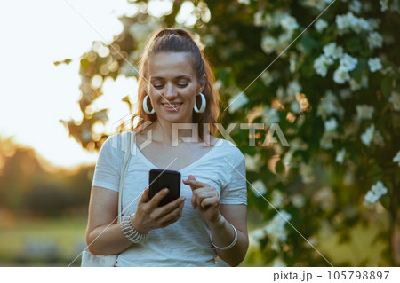 smiling trendy woman in white shirt using smartphone app smiling trendy woman in white shirt using smartphone app 105798897