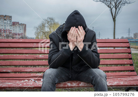 The addict sits alone and depressed on the street, covering his face with his hands. The addict sits alone and depressed on the street, covering his face with his hands. 105799276