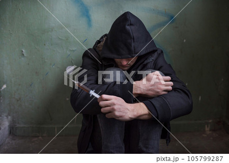 Photo of a desperate young drug addict in the hood and sitting Photo of a desperate young drug addict in the hood and sitting 105799287