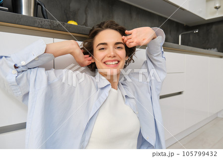 Close up portrait of beautiful smiling woman, stretching hands with pleased face, feels tired, sits on kitchen floor at her home Close up portrait of beautiful smiling woman, stretching hands with pleased face, feels tired, sits on kitchen floor at her home 105799432