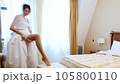 bride fees. beautiful, smiling bride, in veil and lace dress, puts on a lace garter on the leg, in a bright elegant bedroom. morning preparation wedding concept. 105800110