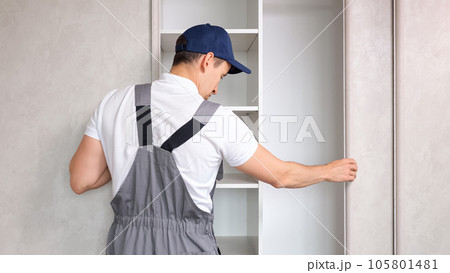 Repairman in uniform inspects broken closet in light bedroom Repairman in uniform inspects broken closet in light bedroom 105801481