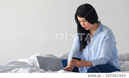 Black-haired woman doing online shopping on laptop from flat 105801483