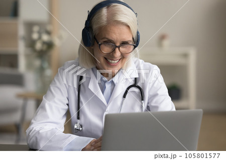 Positive senior doctor in headphones speaking on online video call 105801577