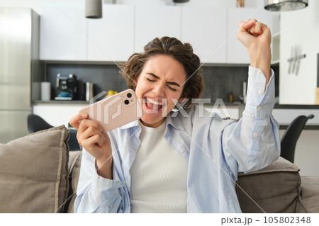 Image of girl celebrating, holding smartphone and cheering from excitement, winning, receive great news on mobile phone 105802348