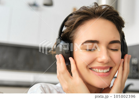 Close up portrait of cute young woman, smiling and listening to music in wireless headphones, enjoying good sound quality 105802396