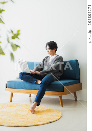 リビングのソファに座ってパソコンを使う若い男性 リビングのソファに座ってパソコンを使う若い男性 105803271