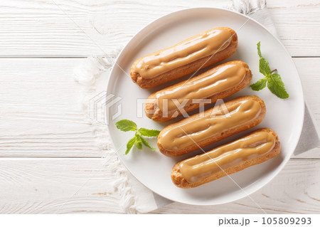 Traditional French dessert Eclairs with custard and topped with caramels icing close-up in a plate. Horizontal top view Traditional French dessert Eclairs with custard and topped with caramels icing close-up in a plate. Horizontal top view 105809293