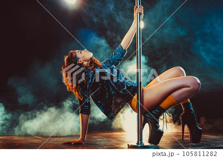 Young woman pole dancing in dark interior with lights and smoke Young woman pole dancing in dark interior with lights and smoke 105811282