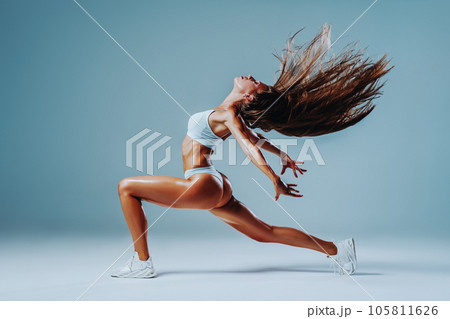 Young fitness woman dancing and shaking hair on white wall background Young fitness woman dancing and shaking hair on white wall background 105811626