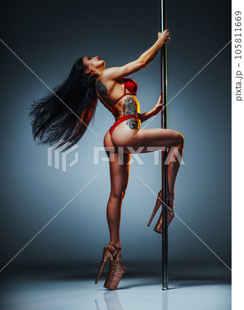 Young brunette woman pole dancing on gray wall background, tattoo on body 105811669