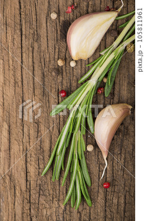 wooden culinary background with garlic, rosemary, bay leaves, pepper and some cloves pictured on it 105811961