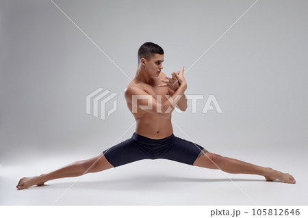 Photo of a handsome man ballet dancer, dressed in a black shorts, making a dance element against a gray background in studio. Photo of a handsome man ballet dancer, dressed in a black shorts, making a dance element against a gray background in studio. 105812646