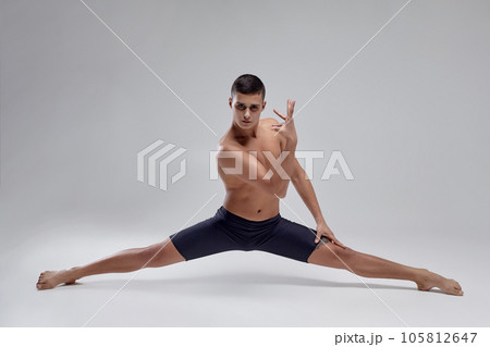 Photo of a handsome man ballet dancer, dressed in a black shorts, making a dance element against a gray background in studio. Photo of a handsome man ballet dancer, dressed in a black shorts, making a dance element against a gray background in studio. 105812647