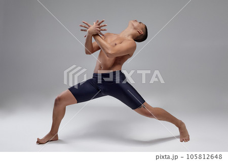 Photo of a handsome man ballet dancer, dressed in a black shorts, making a dance element against a gray background in studio. Photo of a handsome man ballet dancer, dressed in a black shorts, making a dance element against a gray background in studio. 105812648