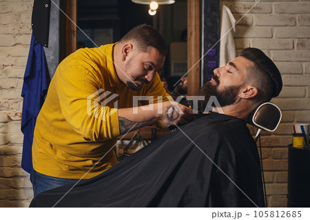 Client with big black beard during beard shaving in barber shop Client with big black beard during beard shaving in barber shop 105812685