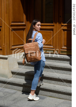 Beautiful young girl wearing blue jeans, shirt and white t-shirt posing with light-brown leather backpack 105814592