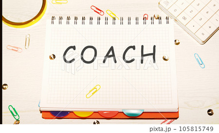 COACH word on a checkered notebook on a light table next to a magnifying glass, paper clips, stationery buttons, a calculator 105815749