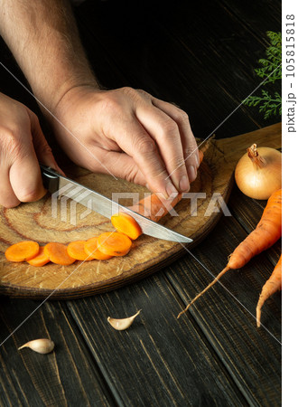 The cook cuts raw carrots with a knife on a wooden cutting board for cooking. Peasant food. 105815818