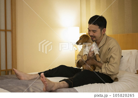 ホテルのベッドで飼い犬と戯れる男性 105820265
