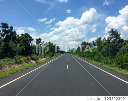 Image of new paved road in the daytime in the countryside painted yellow dividing line with trees, grass along the road, sky with white clouds Image of new paved road in the daytime in the countryside painted yellow dividing line with trees, grass along the road, sky with white clouds 105820309