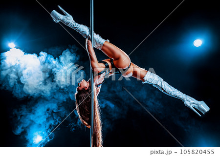 Young woman pole dancing on dark background with blue smoke 105820455