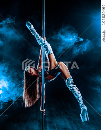 Young woman pole dancing on dark background with blue smoke 105820460