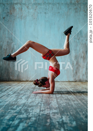 Young woman gymnast standing upside down on gray wall background Young woman gymnast standing upside down on gray wall background 105820670