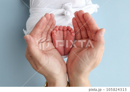 The palms of the father, the mother are holding the foot of the newborn baby on blue background. Feet of the newborn on the palms of the parents. Photography of a child's toes, heels and feet The palms of the father, the mother are holding the foot of the newborn baby on blue background. Feet of the newborn on the palms of the parents. Photography of a child's toes, heels and feet 105824313
