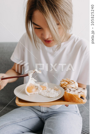 Vertical photo of woman eating fried eggs as breakfast. 105825240