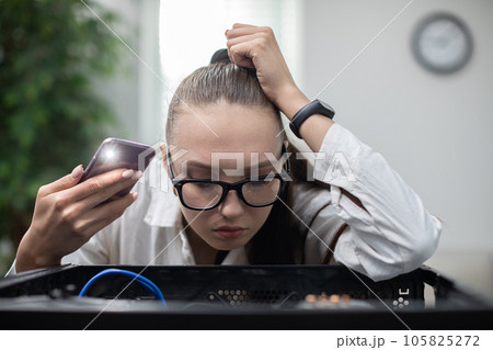 Young woman tries to locate computer failure by shining a flashlight 105825272