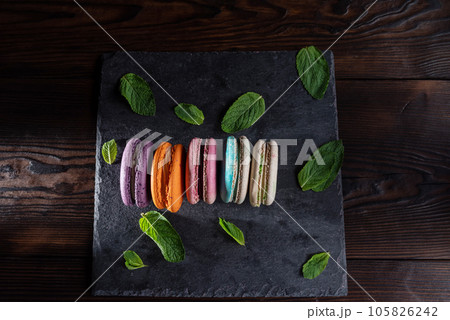 Macaroons of different colors and leaves lie on a slate bottom. Serving sweet macaroons. Sweet French dessert. Macaroons of different colors and leaves lie on a slate bottom. Serving sweet macaroons. Sweet French dessert. 105826242