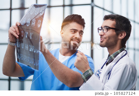 Male medics consult with each other while looking at x ray image. Male medics consult with each other while looking at x ray image. 105827124