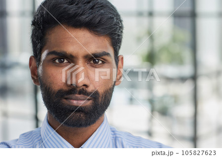 Close up portrait of young attractive serious guy in blue shirt looking straight in the camera 105827623