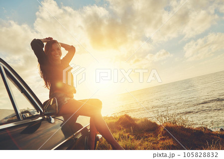 Woman, sunset portrait and road trip on hood of car with smile, beach or happiness for summer vacation. Happy gen z girl, sky and sunshine with nature, outdoor adventure and holiday by ocean in Miami 105828832