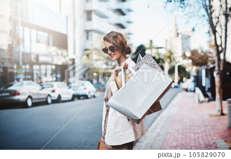 Shopping, spending and consumerism with a female shopper enjoying retail therapy in the city during the day. Young woman carrying bags, looking for a sale or bargain while visiting a shop or store 105829070