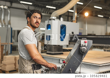 Young carpenter operating machine for wood processing at a furniture factory Young carpenter operating machine for wood processing at a furniture factory 105829481
