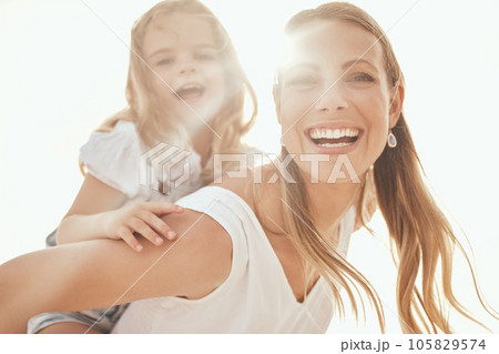 Happy caucasian mother and playful daughter having fun together in the sun. Carefree woman carrying excited girl for a piggyback ride while bonding outside. Single mom enjoying quality time with kid 105829574