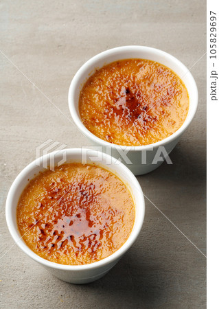 Creme brulee with caramel in two white bowls on gray background Creme brulee with caramel in two white bowls on gray background 105829697