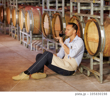 Cellar, mature man wine tasting and sitting by a barrel in a warehouse. Wood cask storage, aging drink and a male sommelier holding or drinking a glass of alcohol or red blend in a factory working Cellar, mature man wine tasting and sitting by a barrel in a warehouse. Wood cask storage, aging drink and a male sommelier holding or drinking a glass of alcohol or red blend in a factory working 105830198