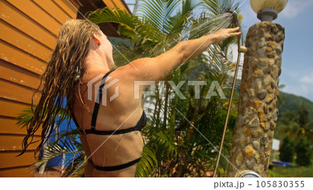 Woman taking a shower in garden near hotel. Girl washes hair, er 105830355